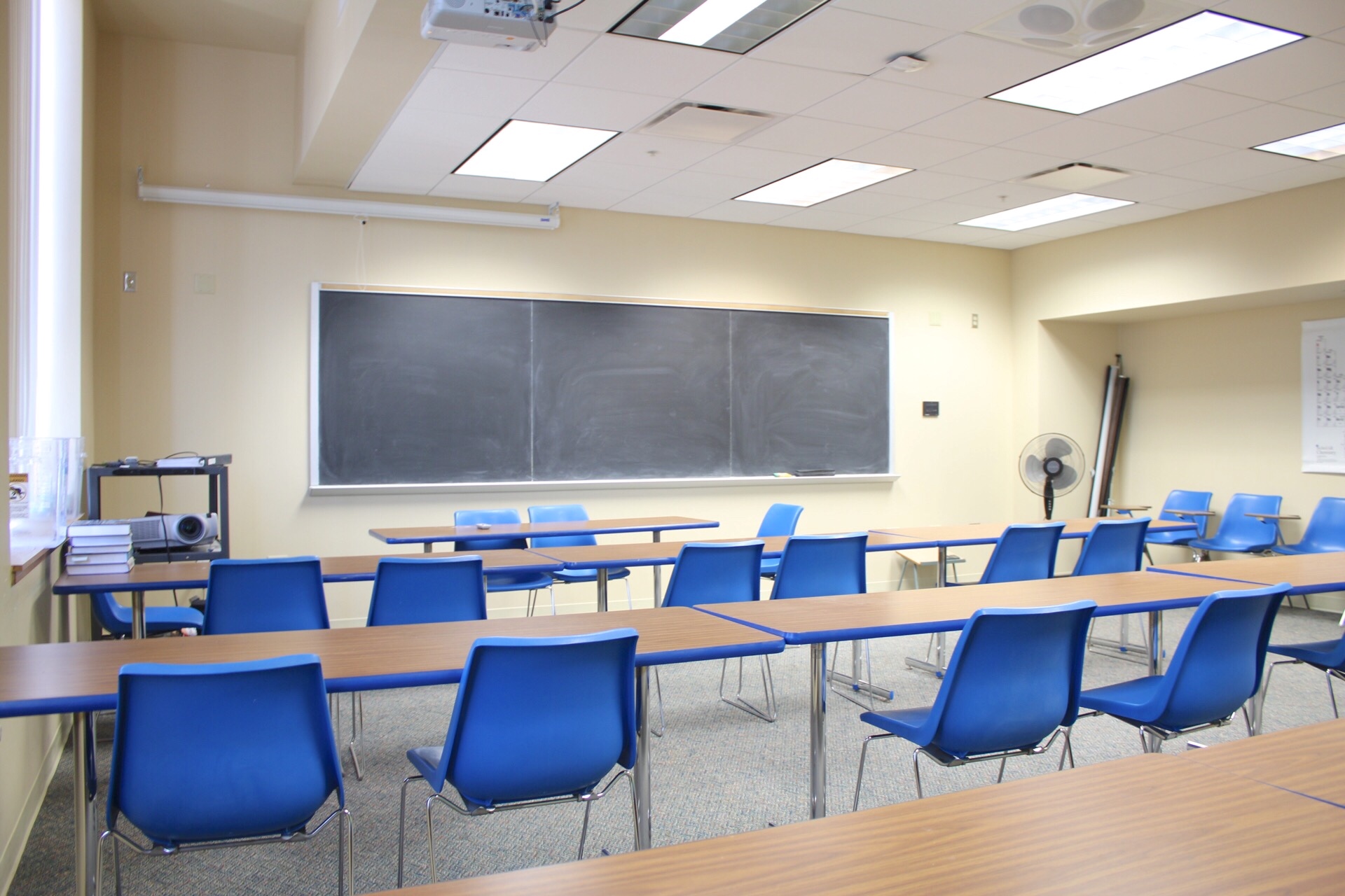 Hoyt讲座307 from back of classroom showing large chalkboard, tables and chairs, projector on a cart, wall mounted projection screen.