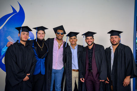 A group of recent graduates in front of the Bobcat logo wall in the AWAC.